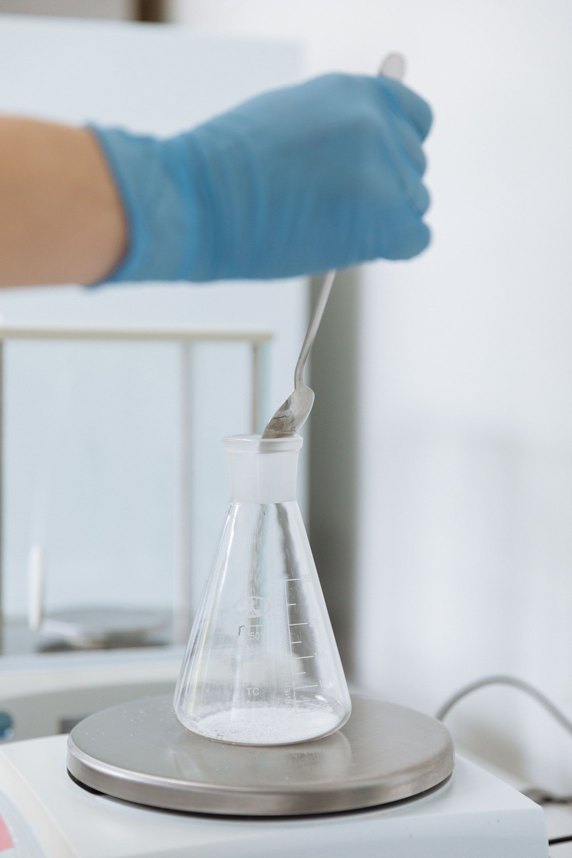 Spatula adding powder to an Erlenmeyer flask on a balance